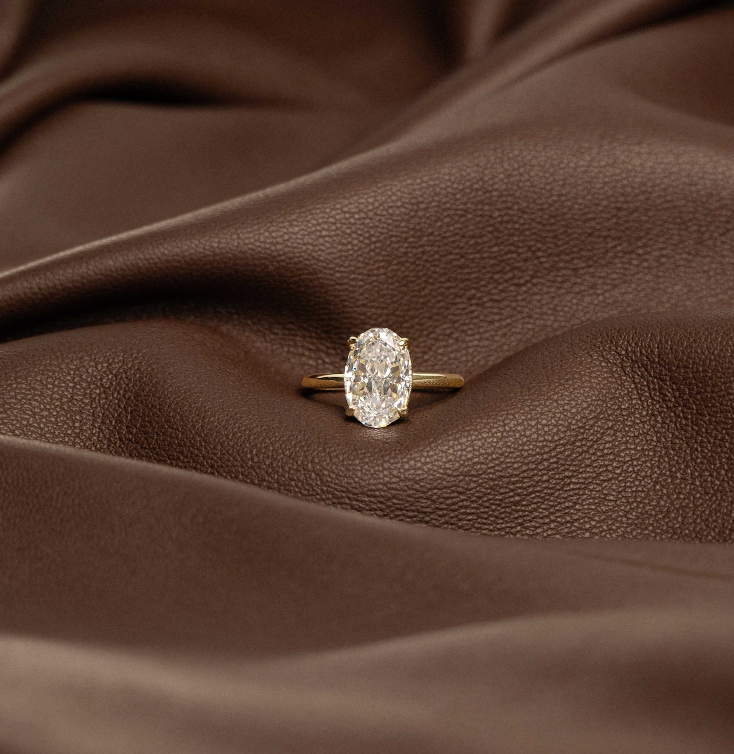 Deus Ring Pherinwen with oval-cut 3-carat moissanite solitaire on brown leather background