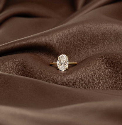 Deus Ring Pherinwen with oval-cut 3-carat moissanite solitaire on brown leather background