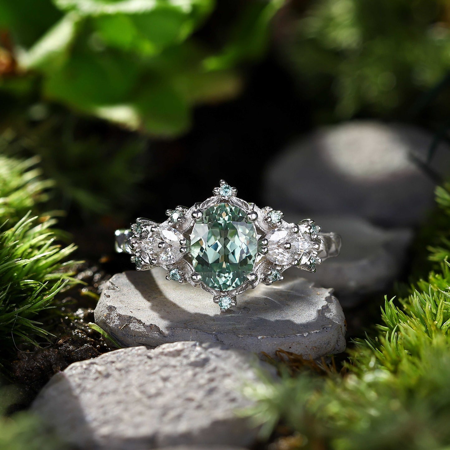 Tyranel engagement ring with oval sapphire and halo of marquise and round moissanite stones on natural stone background