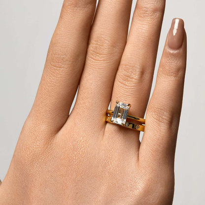 Hand wearing a sleek gold Emera Ring with an emerald-shaped moissanite stone on a plain band