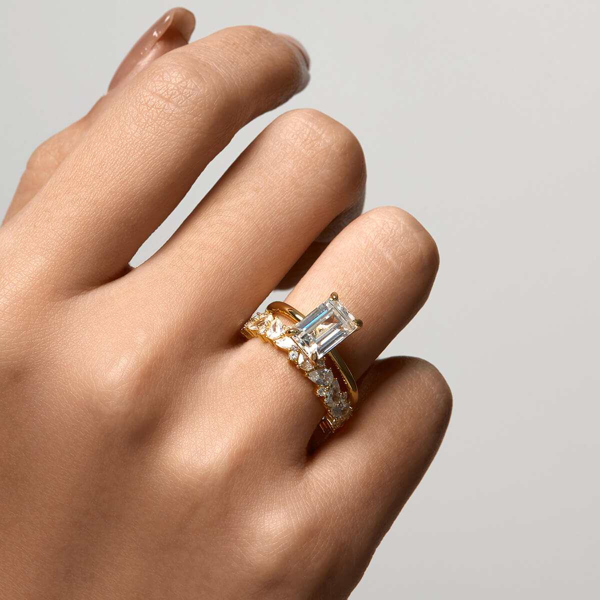 Close-up of hand wearing Beleria emerald-shaped moissanite solitaire ring with gold band and accent stones