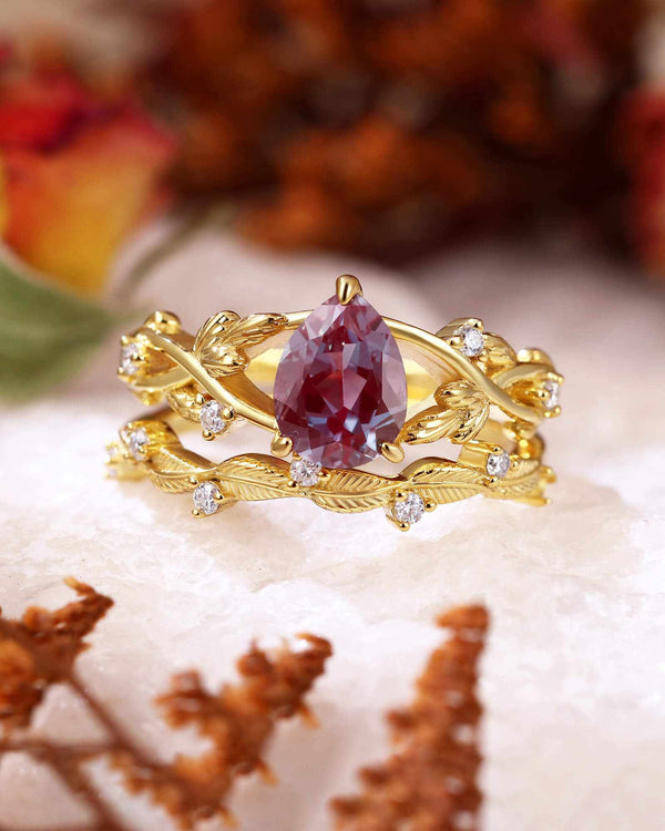Dorelith pear-shaped Alexandrite ring with moissanite side stones and leafy gold band on white surface