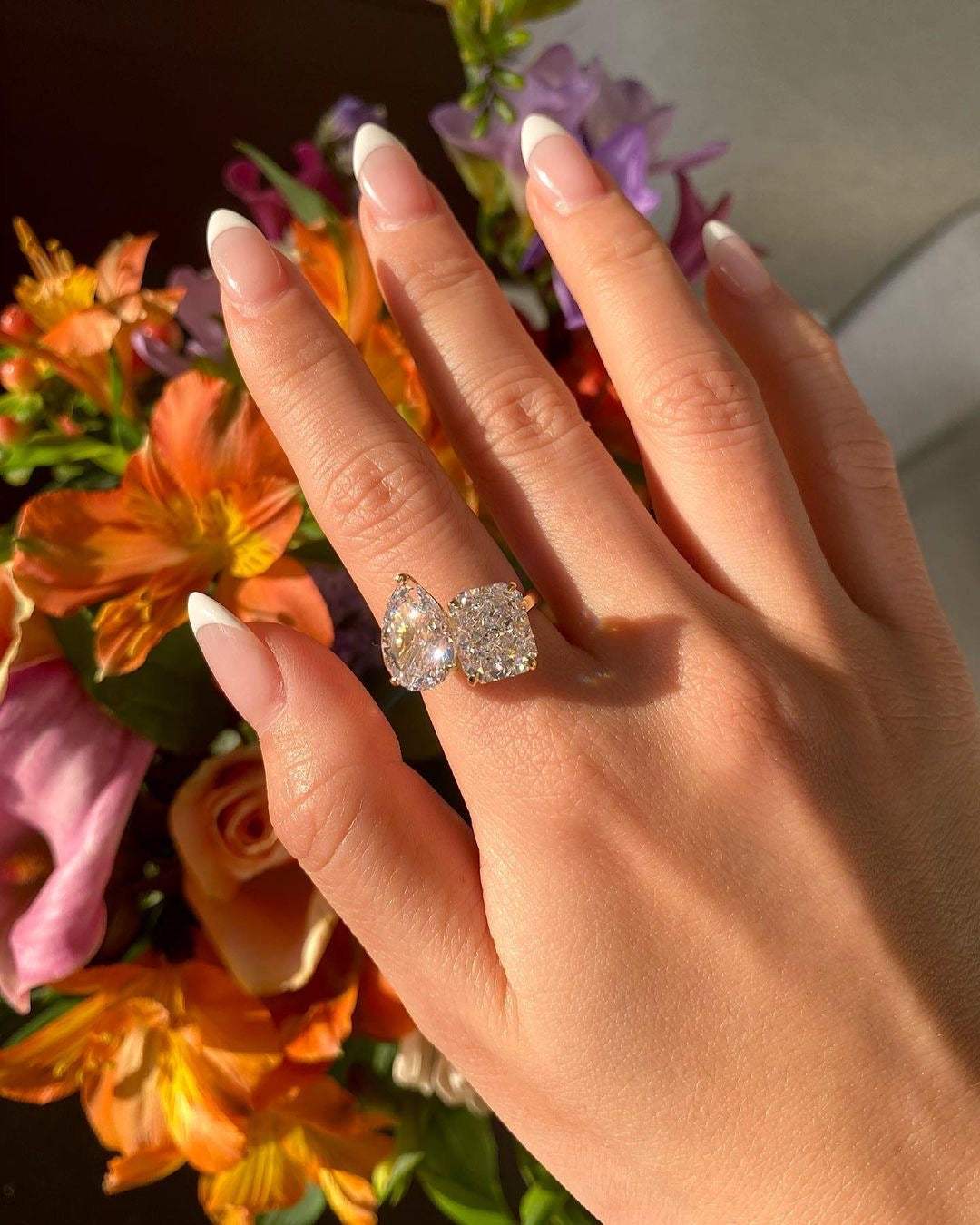 Lalinor engagement ring with two pear-shaped moissanite stones on finger against floral background