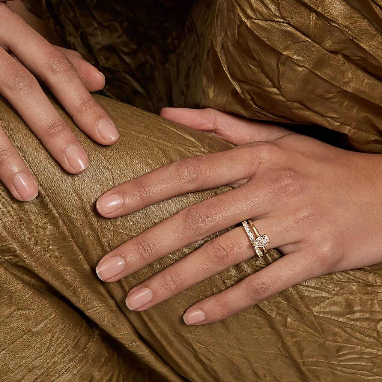 Selene eternity ring with petite round moissanite stones on hand against gold fabric background