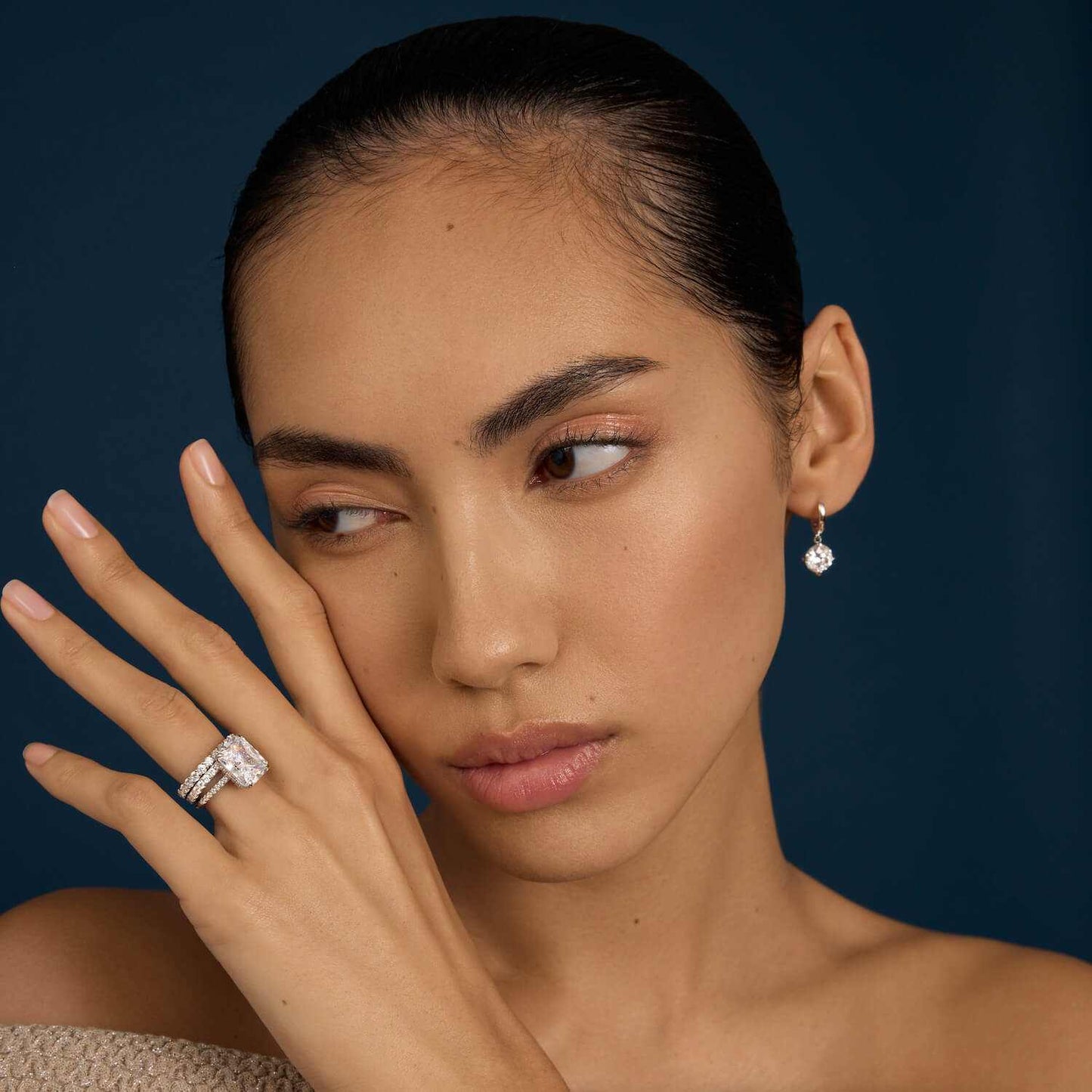 Woman wearing Selene eternity ring with petite round moissanite stones and matching earring on dark background