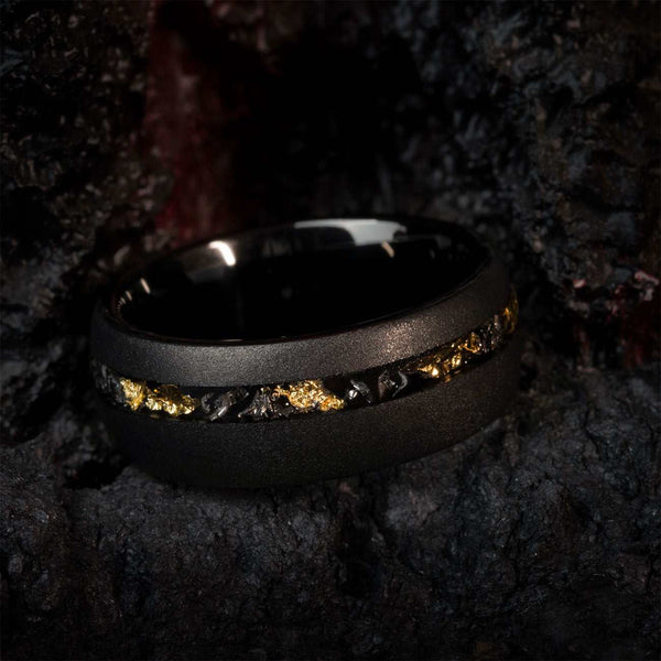 Falneria black tungsten carbide wedding ring with 22k gold leaf and meteorite inlay on dark textured background