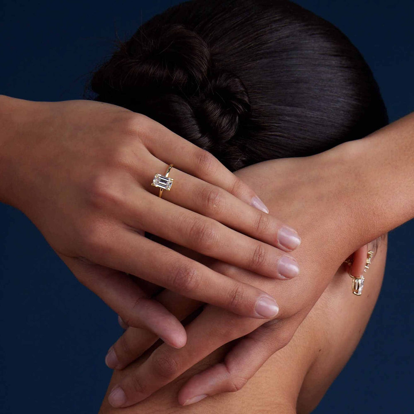 Emera Ring with emerald-shaped moissanite on sleek plain band worn on hand against dark background
