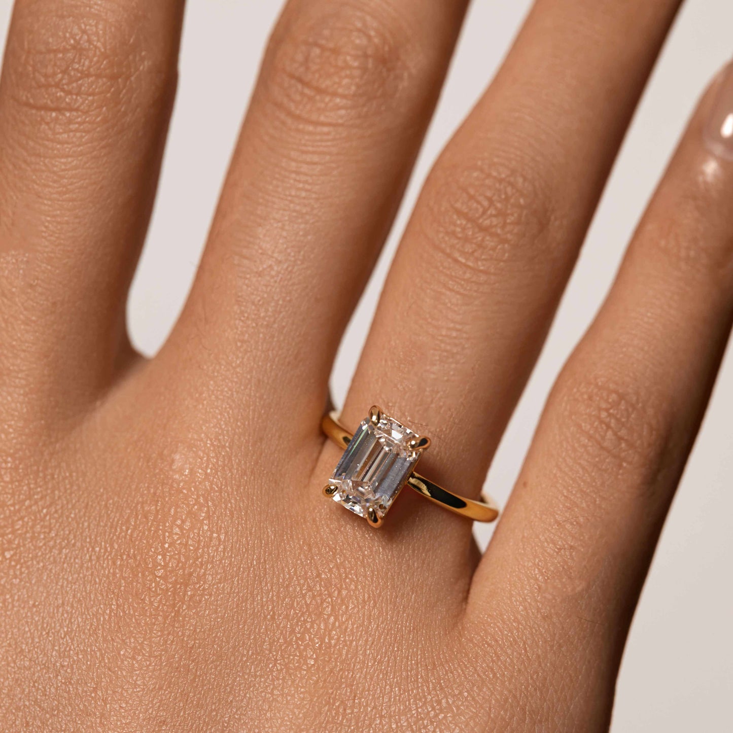Emera Ring with emerald-shaped moissanite stone on gold band worn on hand