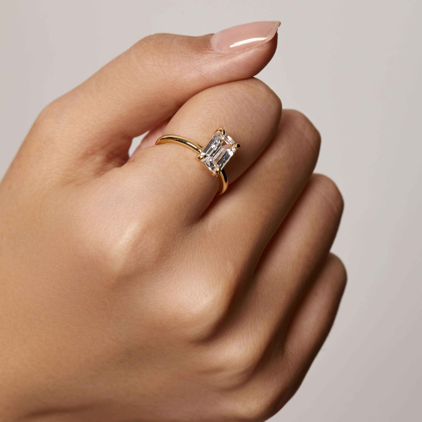Emera ring with emerald-shaped moissanite stone on plain gold band worn on hand