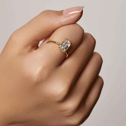 Emera ring with emerald-shaped moissanite stone on plain gold band worn on hand
