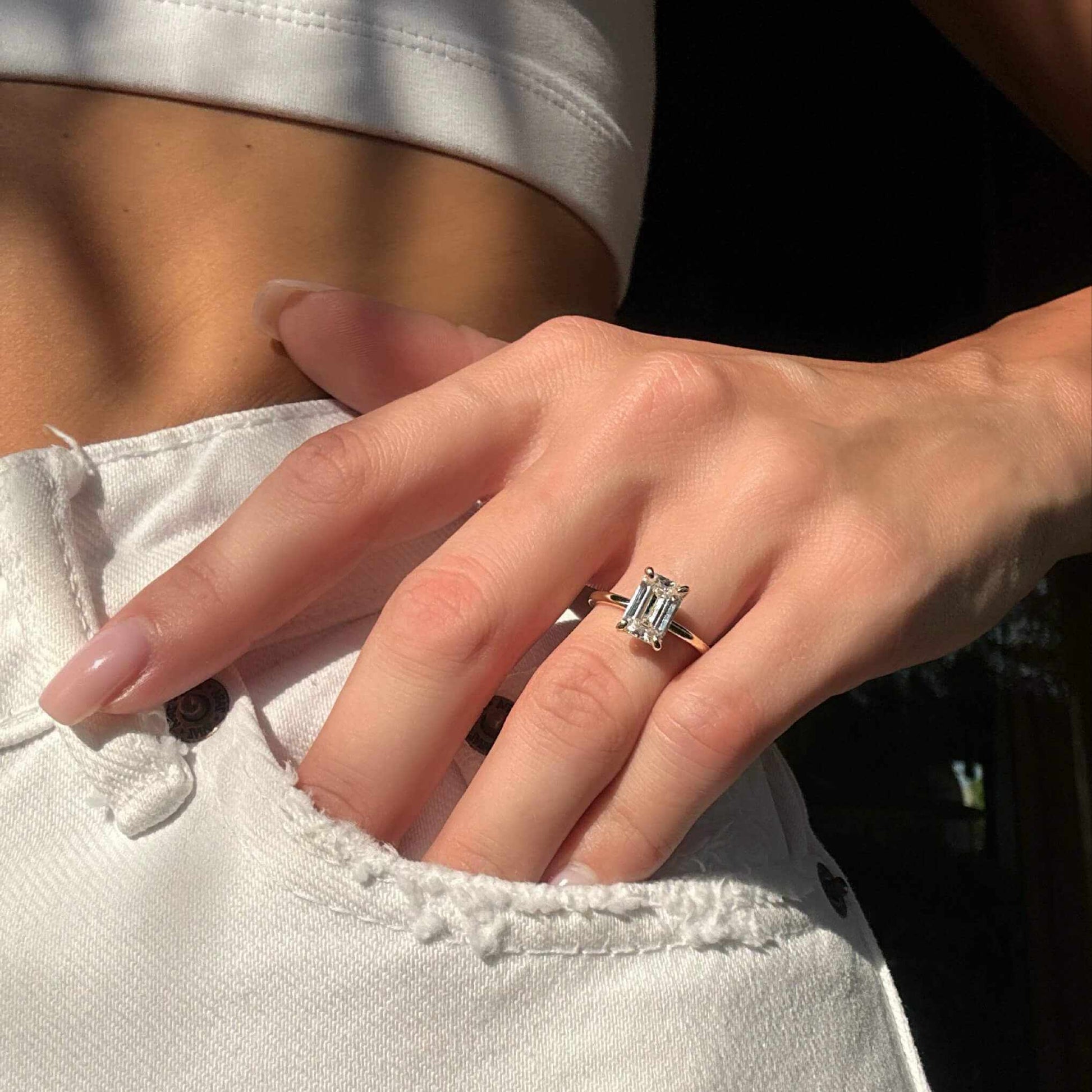 Emerald-shaped moissanite solitaire ring on hand with plain band and hand-finished detail, showcasing the Emera Ring design.