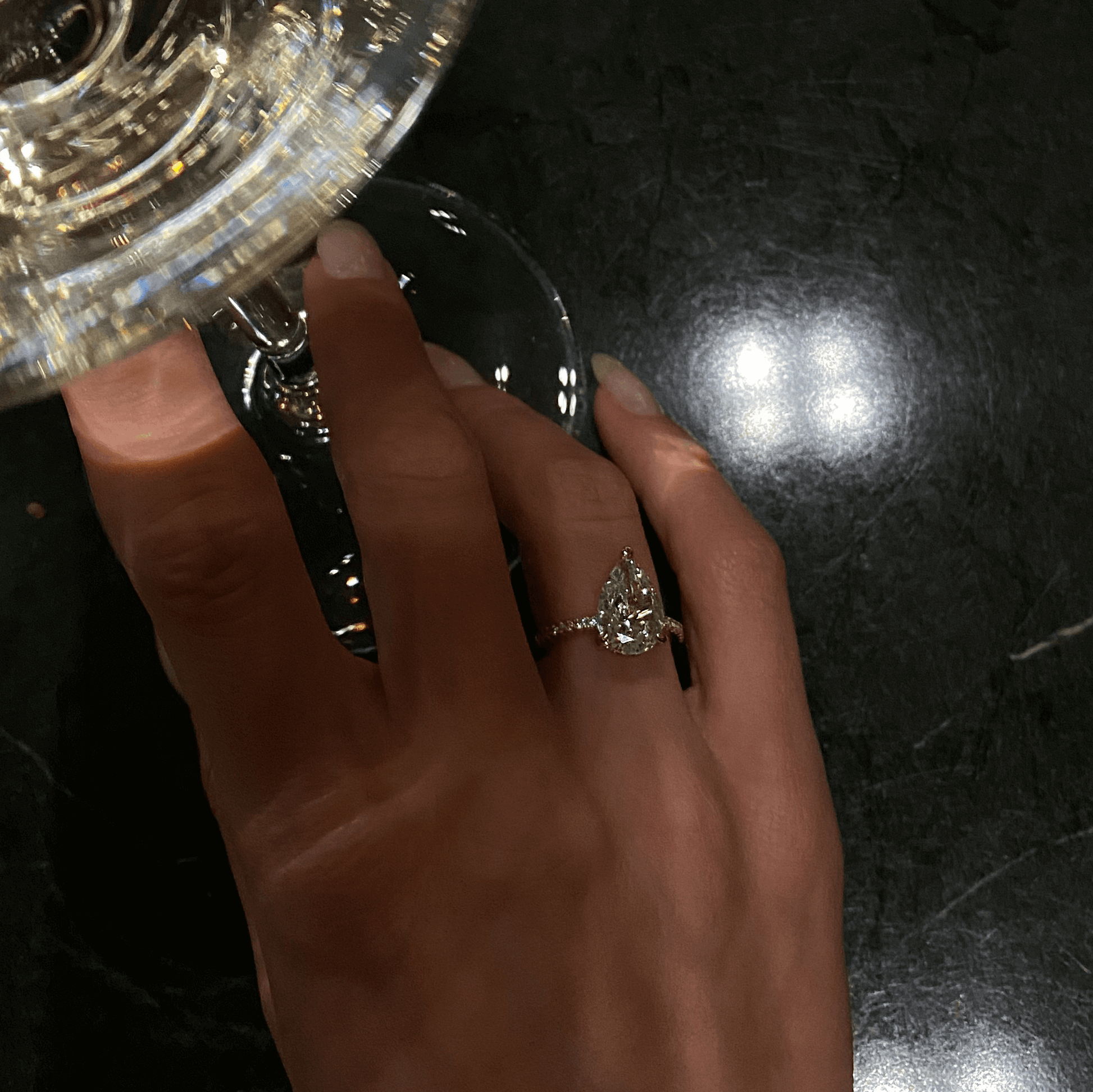 Kylariel pear-shaped moissanite engagement ring with half pavé and hidden halo on hand holding glass
