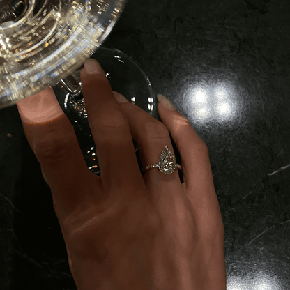 Kylariel pear-shaped moissanite engagement ring with half pavé and hidden halo on hand holding glass